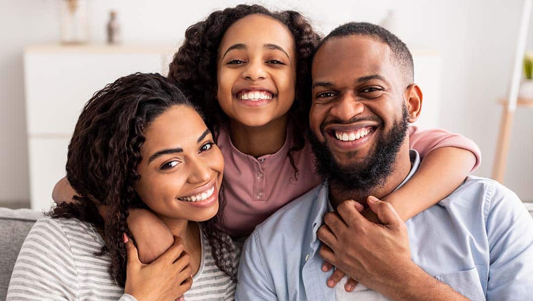 Portrait of a family with a child sitting on their couch, smiling to the camera.