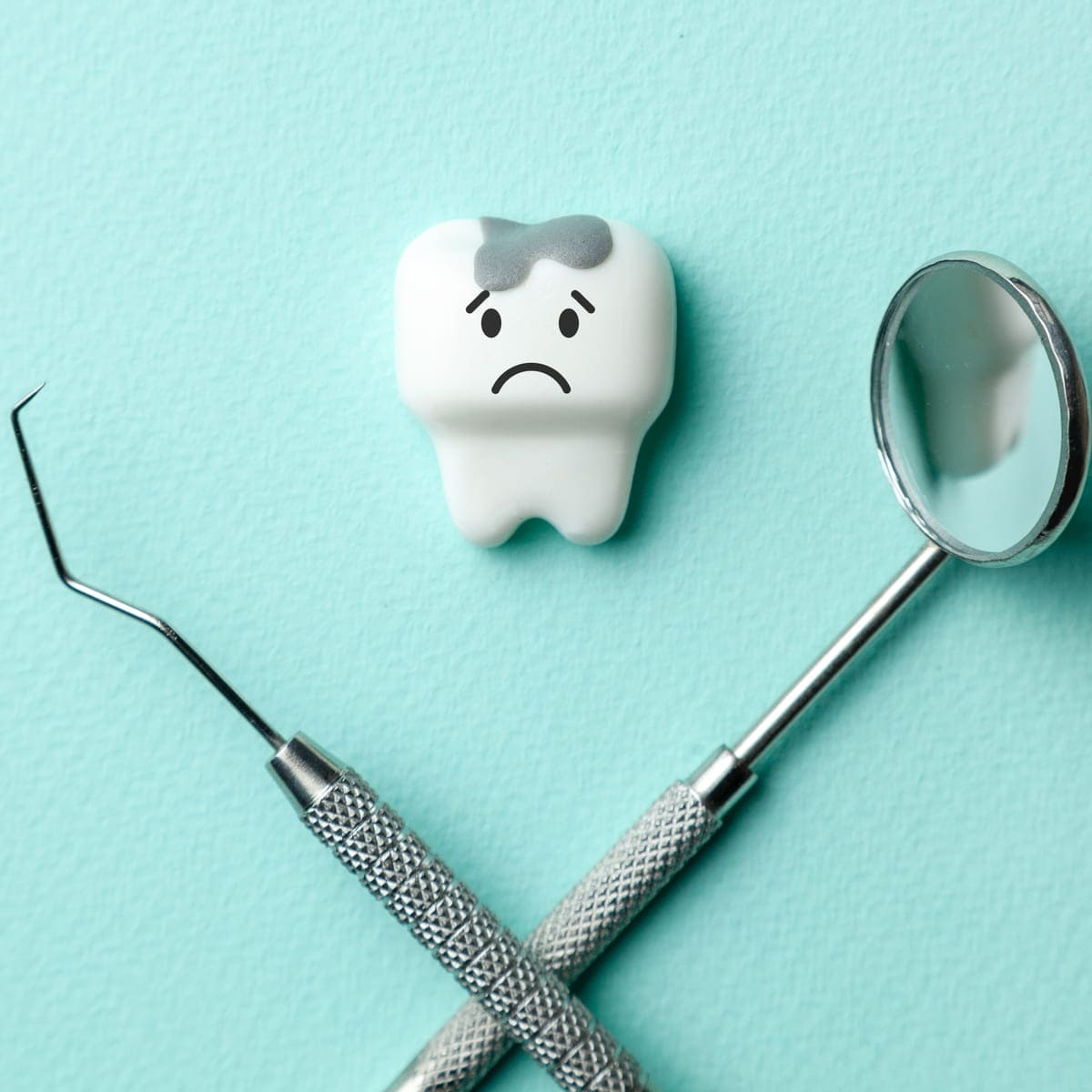 White tooth with caries is sad on green mint background and dentist tools mirror, hook
