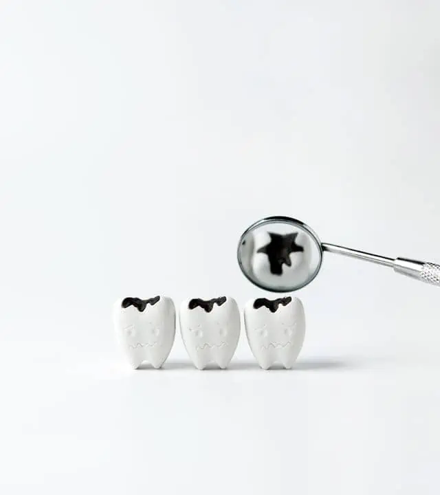 3 small tooth figures with black spots on top and a dental mirror