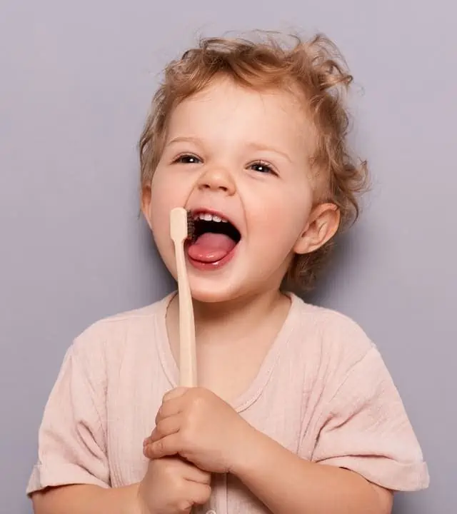 young child smiling with visible teeth, holding a tooth brush