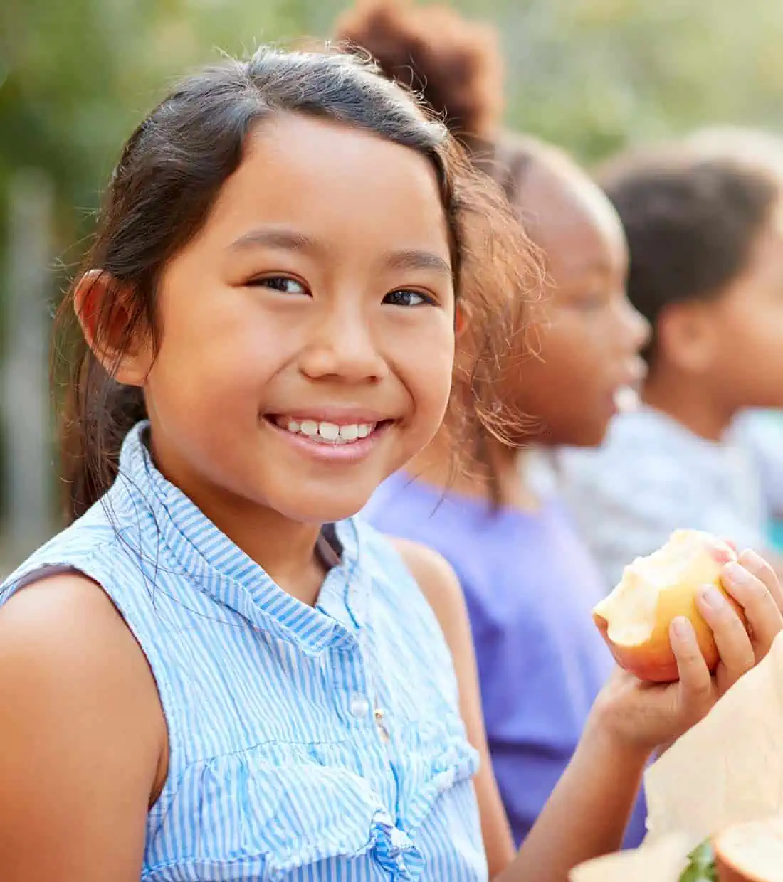 Young girl smiling at the camera with an apple in one hand